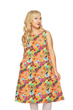 A woman with long blonde hair wears the Cissi och Selma klänning Lill Fågeltivoli Orange by BUTIK KUBIK, standing against a white background, smiling gently, with one hand in the pocket of her colorful floral dress.