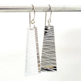 Favoretro earrings sketch by BUTIK KUBIK are two rectangular, clear plexiglass earrings featuring etched diagonal and horizontal lines. They hang on a silver rod against a plain white background, their sleek design enhanced with surgical steel findings.