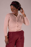 A woman wearing the Emmy - The delightful daytime cardi Peach by BUTIK KUBIK and high-waisted maroon pants smiles as she adjusts her dark hair, styled with a maroon headband, against a plain neutral background.