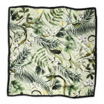 The BUTIK KUBIK Sneaky fox silk scarf Fern features a green floral print with leaves, ferns, white flowers, and yellow birds on a light background, finished with a slim black border.