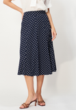A woman wears a white blouse and the navy Jumperfabriken Skirt Sunvi by BUTIK KUBIK, featuring polka dots and midilängd, paired with brown heeled sandals. The image is cropped at her shoulders.