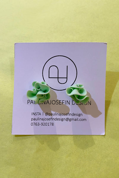 A pair of light green, ruffled Paulina Josefin design earrings by BUTIK KUBIK are displayed on a branded card with logo and contact details, set against a pale yellow background.