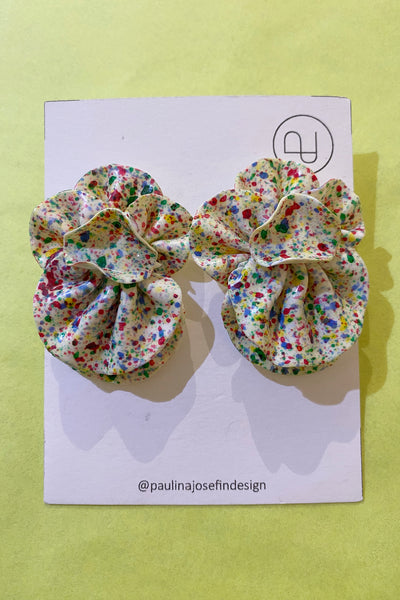 Paulina Josefin design earrings by BUTIK KUBIK—round, fabric with ruffled texture and colorful paint splatters—displayed on a card with @paulinajosefindesign handle, pop against a light yellow background.