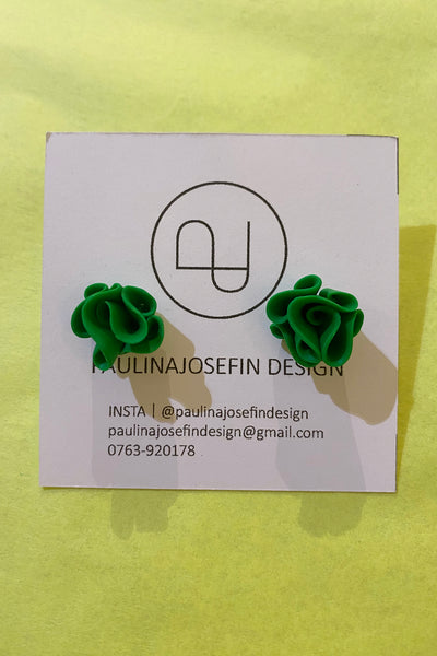 A pair of green rose-shaped Paulina Josefin design earrings by BUTIK KUBIK in polymer clay are displayed on a white card with logo and contact details, set against a yellow background.