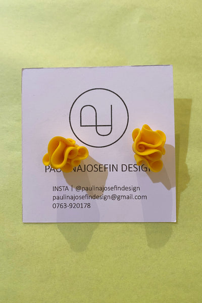 A pair of yellow, flower-shaped Paulina Josefin design earrings by BUTIK KUBIK are shown on a branded card with logo and contact info, set against a pale yellow background.