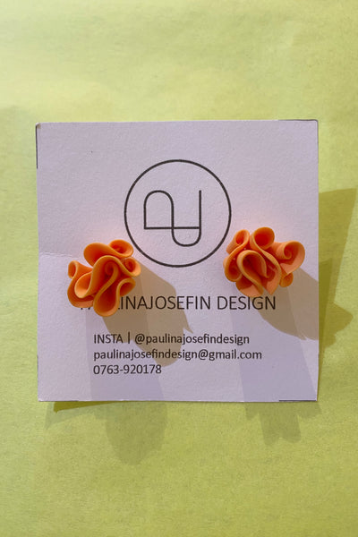 A pair of orange, ruffled Paulina Josefin design earrings by BUTIK KUBIK are shown on a branded business card with contact details and a minimalist logo, against a pale yellow background. Handmade from polymer clay.