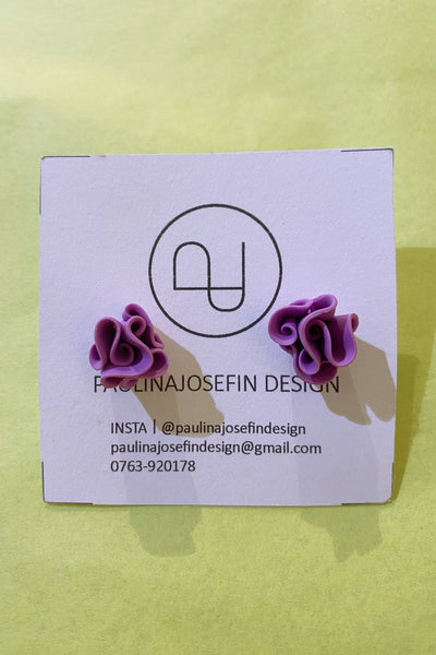 A pair of purple, abstract-shaped Paulina Josefin design earrings by BUTIK KUBIK in polymer clay are shown on a branded card with contact details, set against a yellow background.