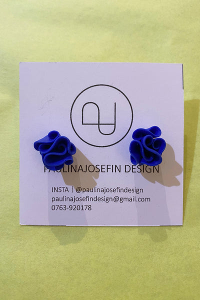 A pair of blue, ruffled Paulina Josefin design earrings from BUTIK KUBIK are displayed on a square card featuring the Paulina Josefin Design logo and contact info, set against a yellow background.