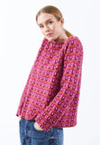 A person with light brown hair in a ponytail wears the BUTIK KUBIK Jumperfabriken Tulipe jumper rose and blue jeans, standing against a plain white background.