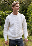A man with blond hair wearing a Jumperfabriken Vide jumper from BUTIK KUBIK stands outdoors in a green, wooded area, looking to the side and smiling.