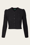The Emmy - The Ice Skater cardigan in black by BUTIK KUBIK is a long-sleeve knit featuring a V-neck, subtle Celtic pattern, ribbed cuffs and hem, front button closure, and slightly puffed shoulders, shown against a plain light background.