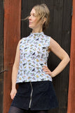 A woman stands before a dark wooden door, wearing the BUTIK KUBIK Kubik top cineast birdie and a black zipper-front skirt, looking confidently to the side.
