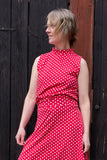 A woman in the Kubik top cineast polkadot red by BUTIK KUBIK stands before a dark wooden wall, looking left with windblown hair.