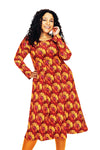 A woman with curly hair smiles in the Cissi och Selma dress Helga Kronblad Vinröd by BUTIK KUBIK, a long-sleeved, knee-length floral höstklänning in soft LENZING ECOVERO viskostrikå, paired with bright orange tights against a white background.