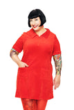 A smiling person with short black hair and tattoos on both arms wears the BUTIK KUBIK Cissi och Selma My velour dress in red, paired with red tights, standing against a white background.