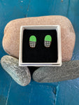 Törmi earrings Verho mini green by BUTIK KUBIK: oval Finnish birch earrings with green tops, black-and-white checkered bottoms, eco-packaged and displayed on smooth stones against a blue wooden background.