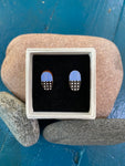 The Törmi earrings Verho mini sky blue by BUTIK KUBIK are oval-shaped Finnish birch earrings, featuring a blue top and black-and-white checkered bottom, presented in eco-friendly packaging and displayed on a stylish white box.