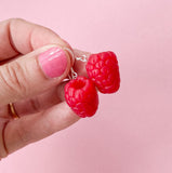 A hand with pink nail polish holds two Becca design Hallon earrings from BUTIK KUBIK, crafted from sterling silver, against a light pink background.