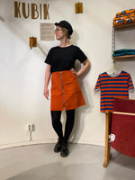 A woman stands in a room wearing the Kubik corduroy zip skirt nr 2 by BUTIK KUBIK, made from Oeko-Tex certified cotton corduroy.