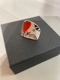 The BUTIK KUBIK Saved & remade ring porslin, a silver-plated white piece with a red heart and black-and-white cat design, elegantly rests on a textured dark gray box. It includes a small black heart, all crafted from remade porcelain on a light-colored surface.