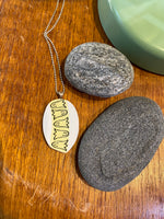 The BUTIK KUBIK Saved & remade necklace Porcelain rests on a wooden surface near two smooth gray stones and a green object in the corner.