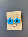 Saved & remade earrings by BUTIK KUBIK: Blue and white flower-shaped pendants made from recycled porcelain, with dark centers and silver-plated hooks. Displayed on a brown card with spiral logo, placed on a gray surface.