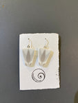 A pair of geometric white Saved & remade earrings by BUTIK KUBIK, featuring gray leaf designs on upcycled porcelain, are shown on a textured card with a spiral logo and “Seeks & Remade”; background is gray.