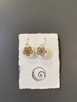 A pair of Saved & remade earrings by BUTIK KUBIK—white silverplated with brown floral designs, made from recycled porcelain, shown on a textured white card with spiral logo and Saved and Remade text, set against a gray background.