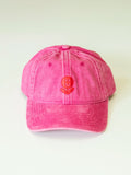 The BUTIK KUBIK Tropical Scandinavia cap pink is a bright pink 100% cotton baseball cap with a faded texture, red embroidered smiley face on the front, and an adjustable brass closure, shown on a plain white background.