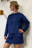 Wearing the BUTIK KUBIK Kubik corduroy overshirt in kobolt, a person with glasses and short hair stands against a plain white wall, one hand on their hip as they look to the side.
