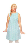 A woman with long blonde hair in a side braid wears the Cissi och Selma dress Rut Petit Turkos from BUTIK KUBIK and red earrings, standing with her hands slightly out to the sides against a white background.