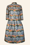 The BUTIK KUBIK Palava Dress Cynthia leaping deer is a knee-length, long-sleeved vintage-style dress with a fitted waist, high collar, and a colorful leaping deer print on a light blue background.