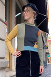 A woman in glasses, a black cap, and the BUTIK KUBIK Kubik cropped sweater waffle patch (size M) poses confidently on a cobblestone street, pairing it with a black skirt with a front zipper.