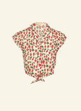 The Palava Peggy blouse Red strawberries by BUTIK KUBIK is a 50s-inspired short-sleeved, button-up shirt with a collar, featuring a red strawberry and green leaf print on cream organic cotton-linen, and a front knot hem.