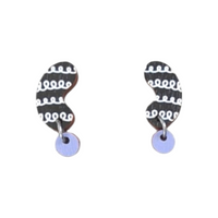 The Törmi papu mini earrings lavender by BUTIK KUBIK showcase black and white abstract wavy shapes on Finnish birch plywood, enhanced by dangling light purple discs at the bottom. They feature surgical steel hooks for comfort and style.