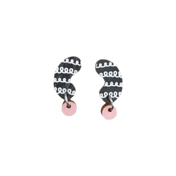 The Törmi papu mini earrings from BUTIK KUBIK are abstract designs crafted from Finnish Birch plywood, featuring black and white wavy patterns with small pink circular pieces at the bottom. They have surgical steel posts and come in eco-friendly packaging.