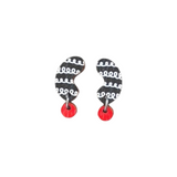 The Törmi Papu mini earrings by BUTIK KUBIK showcase asymmetrical black shapes with white swirls, attached to small red circles. Made from Finnish Birch plywood and finished with surgical steel hooks, they come in eco-friendly packaging for sustainability.