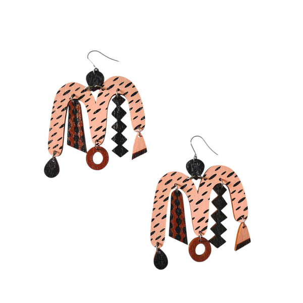 The Törmi Karnevaali earrings pink/brown by BUTIK KUBIK are abstract, multicolored Finnish Birch plywood earrings with pink, brown, and black geometric patterns and metallic hooks. Eco-friendly packaging included.
