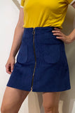 Person wearing a yellow short-sleeve top and the BUTIK KUBIK Kubik corduroy zip skirt nr 1 kobolt, featuring front pockets and a center zipper, standing against a light background.
