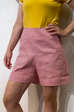 A person wearing a yellow top and BUTIK KUBIK Kubik workwear shorts made from vintage fabric with red-and-white vertical stripes stands with one hand on their hip against a plain white background.
