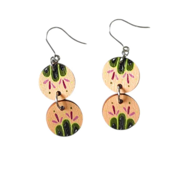 The Törmi Satu earrings floral by BUTIK KUBIK are handmade Finnish birch plywood earrings with two round light wood discs, green and black leaf patterns, pink accents, silver hooks, and eco-friendly packaging.