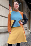 A woman poses on a cobblestone street wearing the BUTIK KUBIK Kubik cropped sweater waffle patch in XL, a 60's-inspired knit top made from organic cotton with color blocking in mustard yellow, blue, black, and rust.