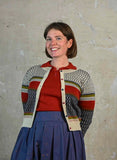 A woman smiles wearing a red polo shirt under a multi-colored Palava Vera Fair Isle Cardigan by BUTIK KUBIK and a blue pleated skirt.
