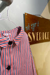 A Kubik Overshirt Strömma Kadett blåröd by BUTIK KUBIK hangs on a white hanger beside a brown "vi syr i SVERIGE" sign on a pale green wall.