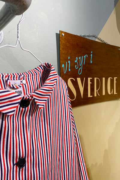 A Kubik Overshirt Strömma Kadett blåröd by BUTIK KUBIK hangs on a white hanger beside a brown "vi syr i SVERIGE" sign on a pale green wall.