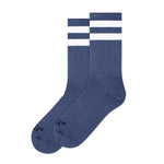 BUTIK KUBIK’s American Socks Mid High Marine are blue crew skate socks with two white stripes near the top, black text at the toe, and a durable, vegan-friendly design. Displayed side by side.