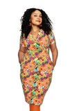 A person with curly hair stands confidently, wearing the Cissi och Selma klänning Betty Fågeltivoli orange from BUTIK KUBIK and orange earrings, set against a plain white background.