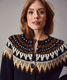A woman with light brown hair wears the Jumperfabriken Cardigan Cilla ny by BUTIK KUBIK, featuring a multicolored geometric yoke in white, brown, and gold. She looks at the camera against a neutral background.