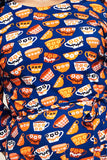 This vibrant fabric features a pattern of orange, yellow, red, and white teacups with floral and geometric designs on a blue background. It is part of the Doris Kittens koppar orange dress by Cissi och Selma from BUTIK KUBIK, inspired by 1960s style and crafted in organic cotton jersey.