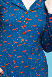 Cissi och Selma dress Viveca Rävar is a blue 70s-style shirt dress featuring a repeating pattern of orange foxes and small yellow flowers, with red buttons down the front.